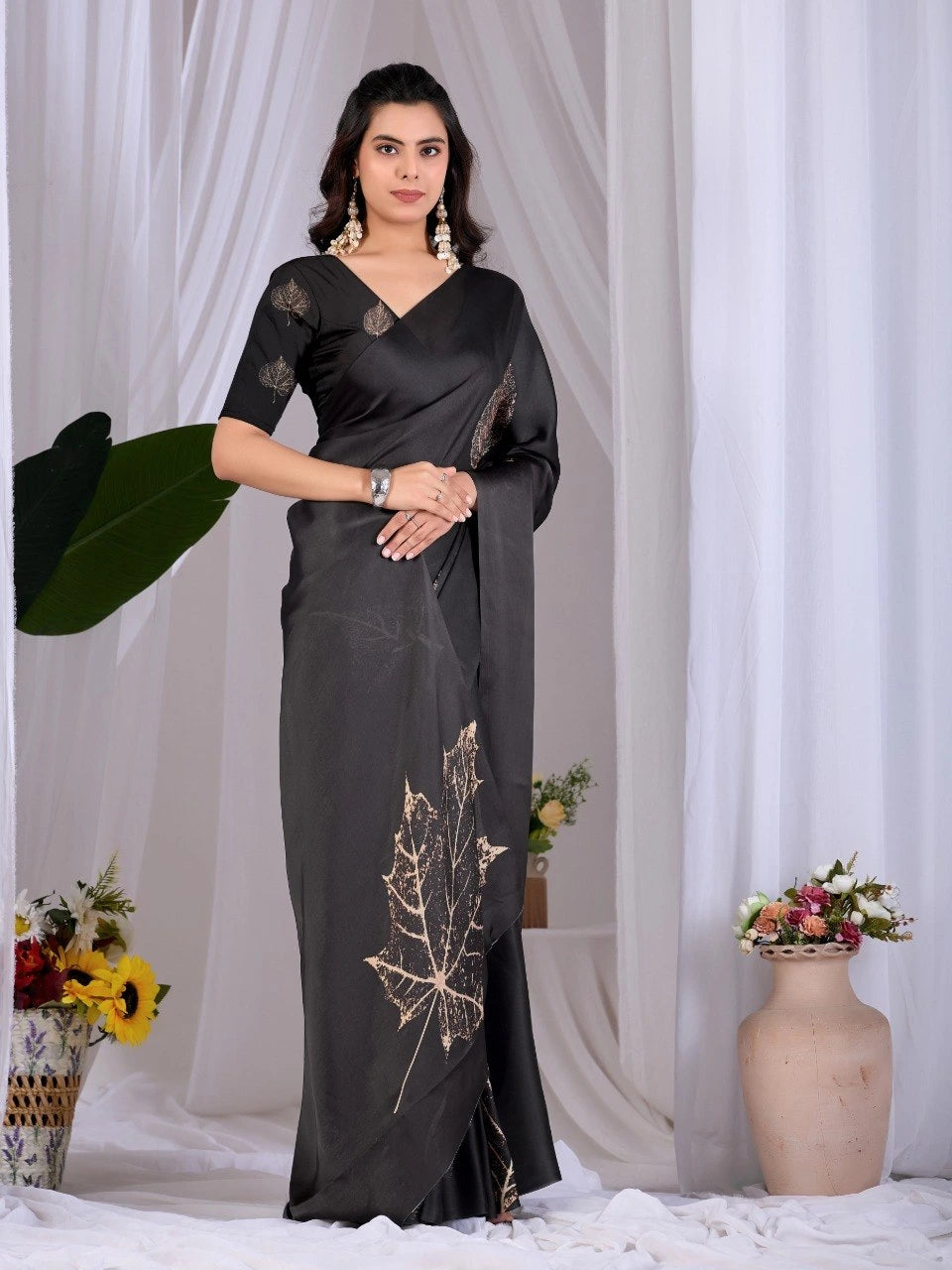 Woman wearing a black saree with gold leaf patterns against a white curtain background