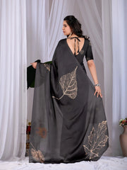 Woman wearing a black saree with leaf patterns against a white curtain background