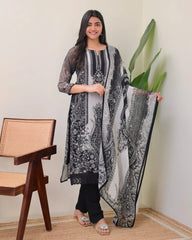 Woman holding a black and white patterned dupatta in a room with a chair and plant.