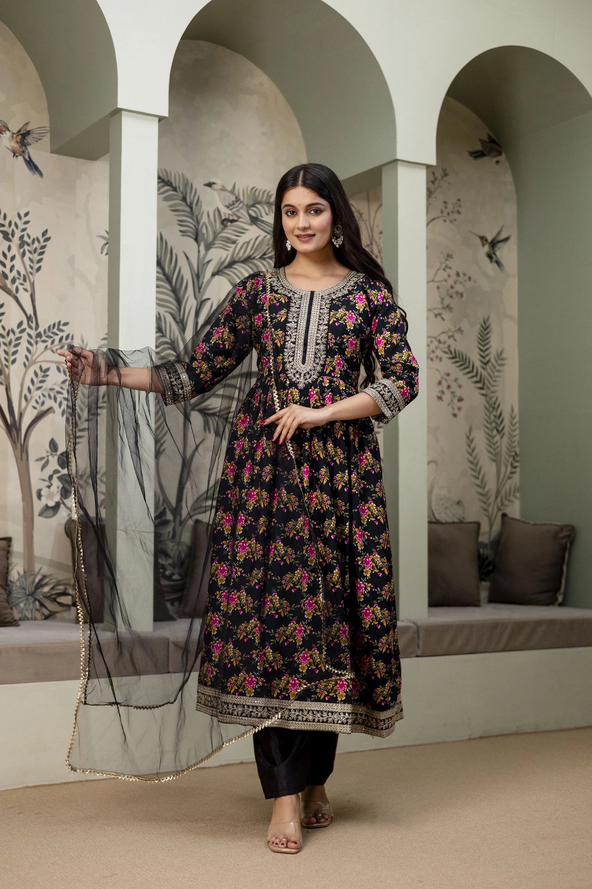 Woman in a floral dress standing in a decorated room with arches and decorative elements.