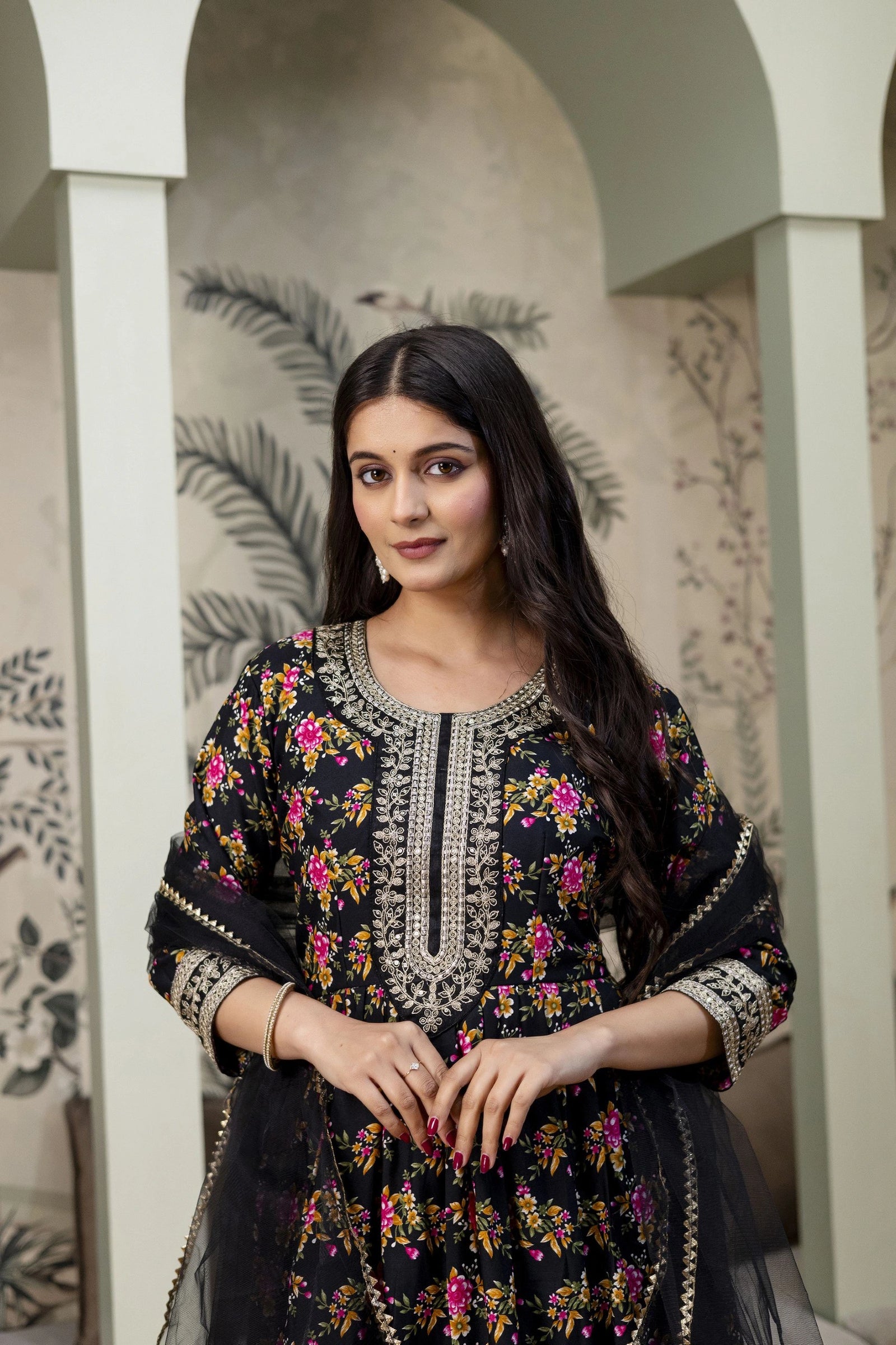 Woman wearing a black embroidered traditional outfit with floral patterns in an indoor setting.