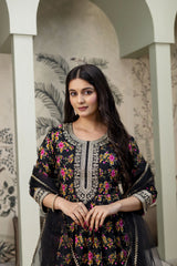 Woman wearing a black embroidered traditional outfit with floral patterns in an indoor setting.