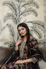 Woman in a floral dress standing against a leaf-patterned wall.
