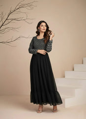 Woman in a black and gray dress standing on a staircase with a beige wall and branch in the background.