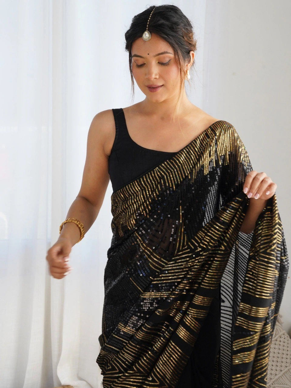 Woman wearing a black and gold saree with a white curtain background