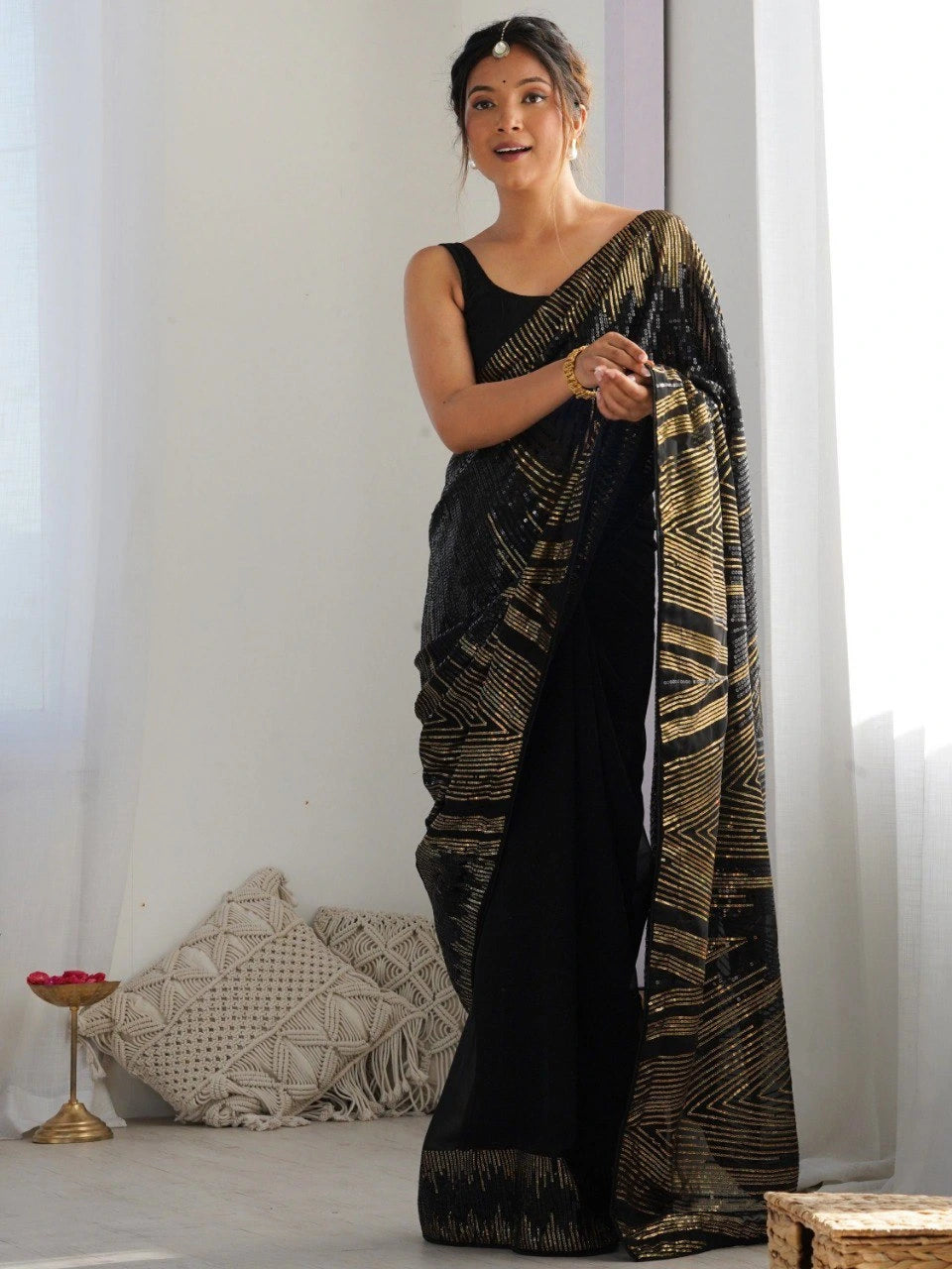 Woman holding a black and gold saree against a white background