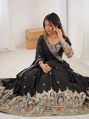 Woman in a black embroidered traditional outfit sitting on a white floor.