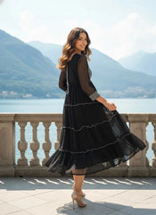 Woman in a black dress standing on a balcony with mountains and water in the background