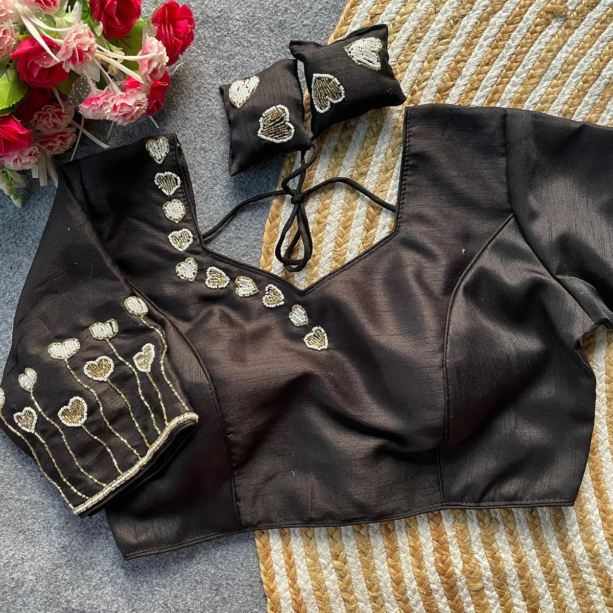 Black blouse with gold embroidery on a textured surface with flowers.
