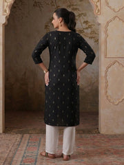Woman wearing a black kurta with white patterns in an ornate room.