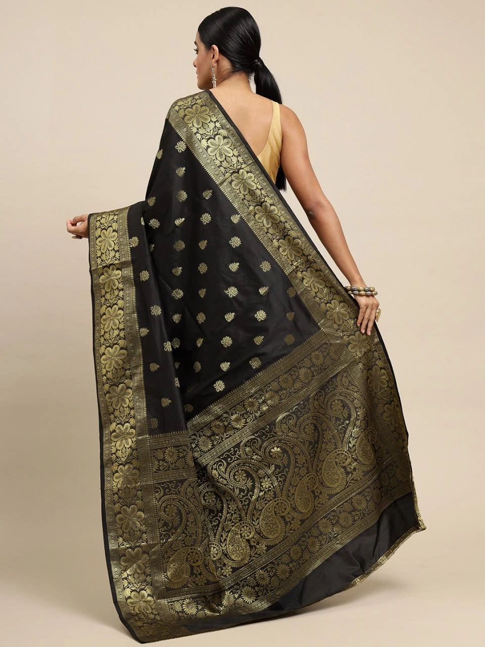 Woman wearing a black saree with gold patterns on a beige background