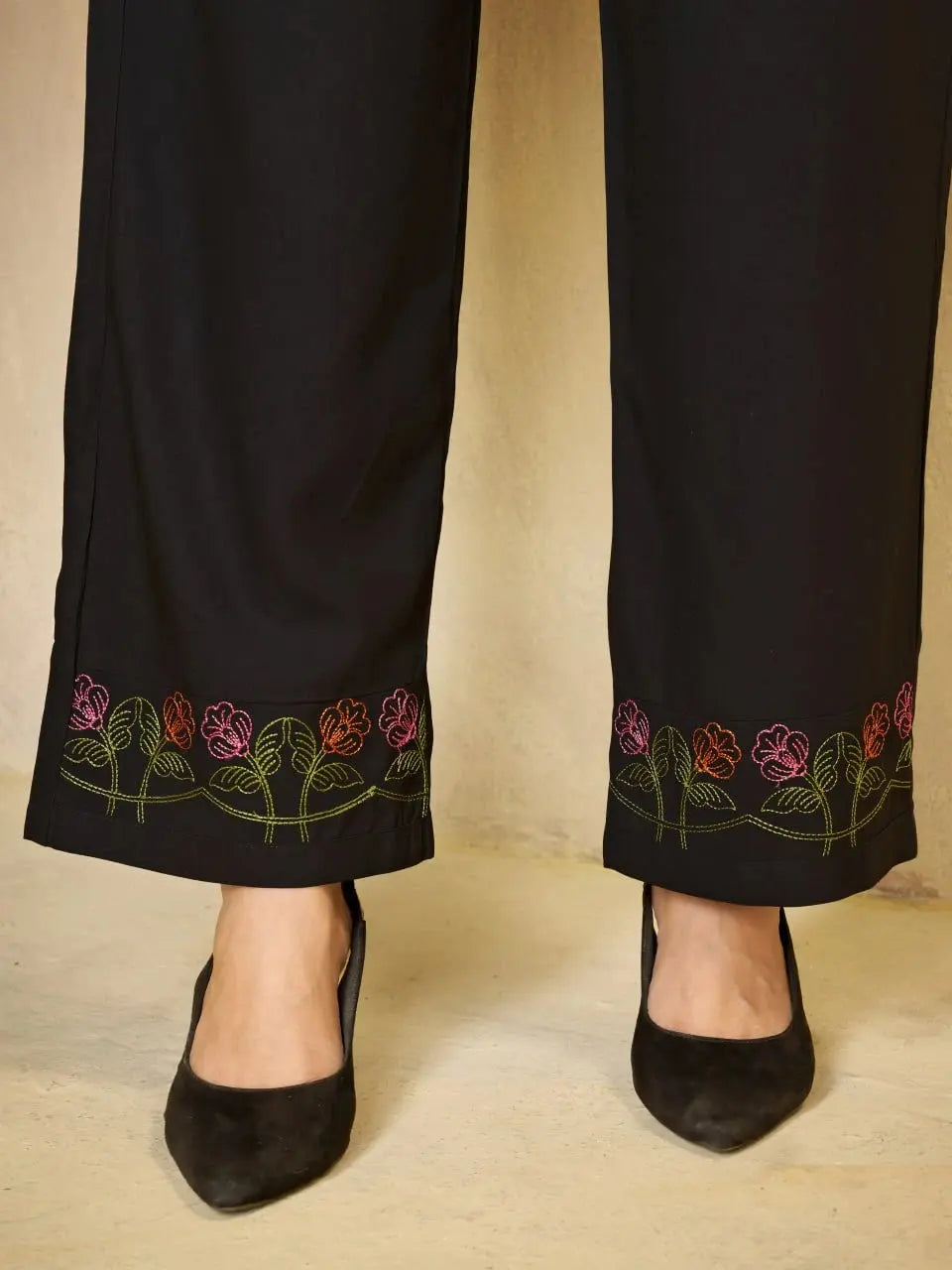 Black pants with floral embroidery at the bottom worn by a person on a beige background