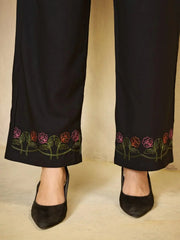 Black pants with floral embroidery at the bottom worn by a person on a beige background