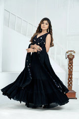 Woman in a black dress with intricate detailing standing against a white background
