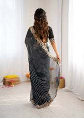 Woman wearing a black saree with gold border in a minimal indoor setting