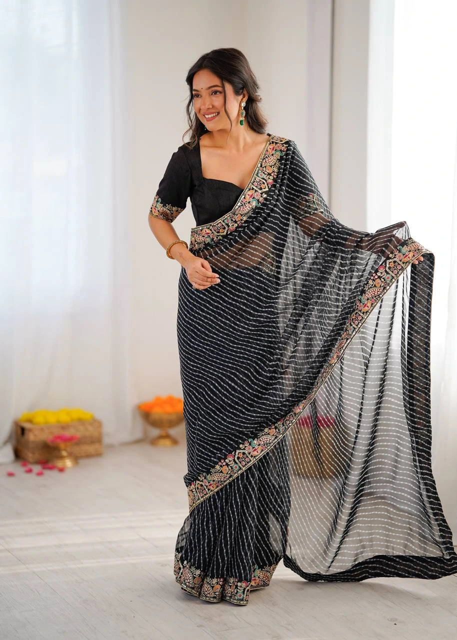 Woman wearing a black saree with a floral blouse, standing indoors.