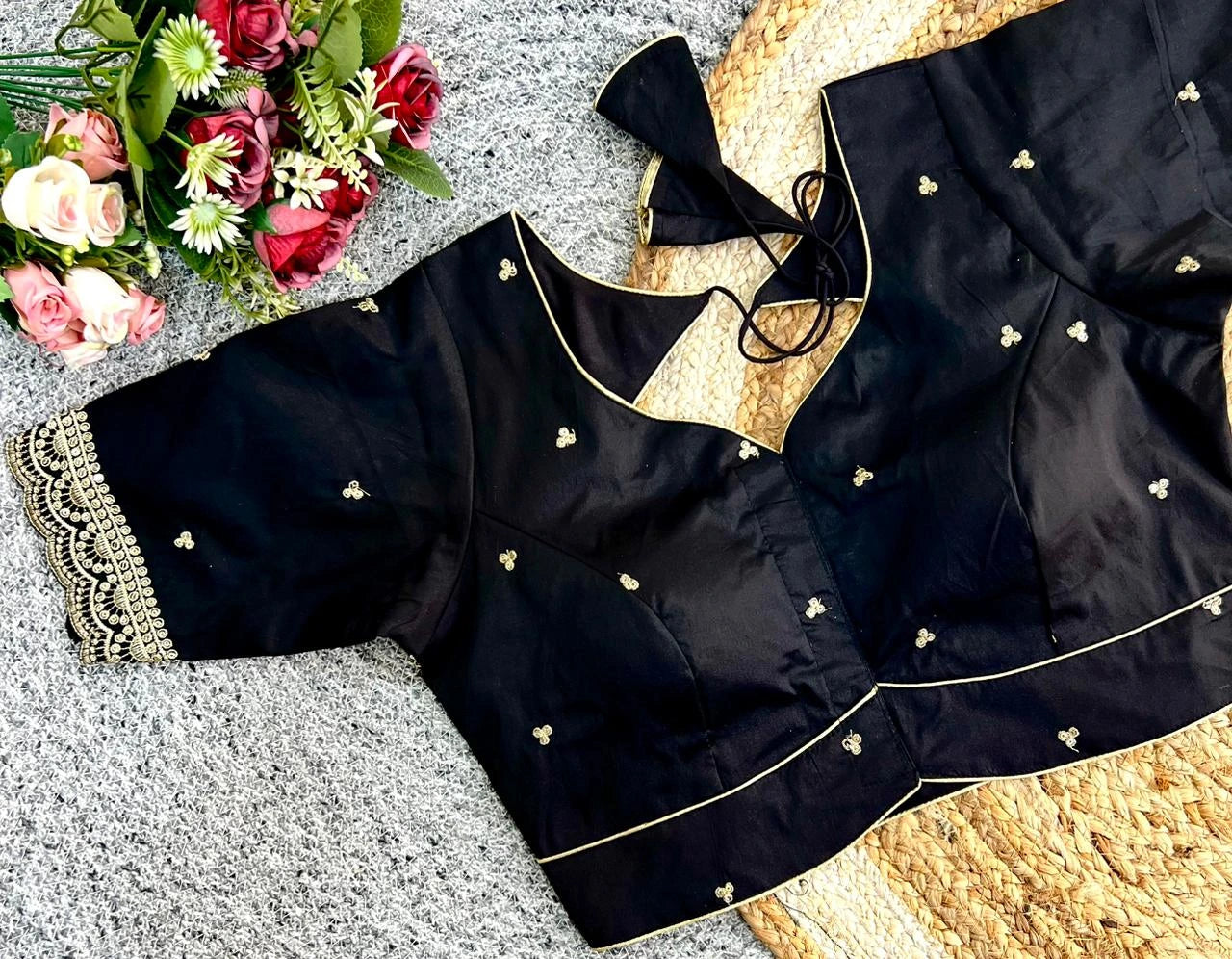 Black blouse with gold embroidery on a textured surface with flowers in the corner