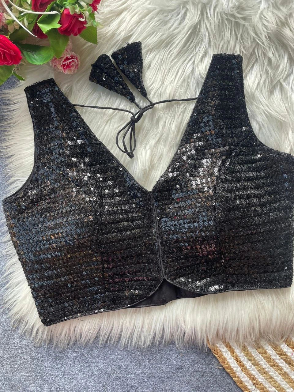 Black sequined bralette on a fluffy white surface with flowers in the corner.