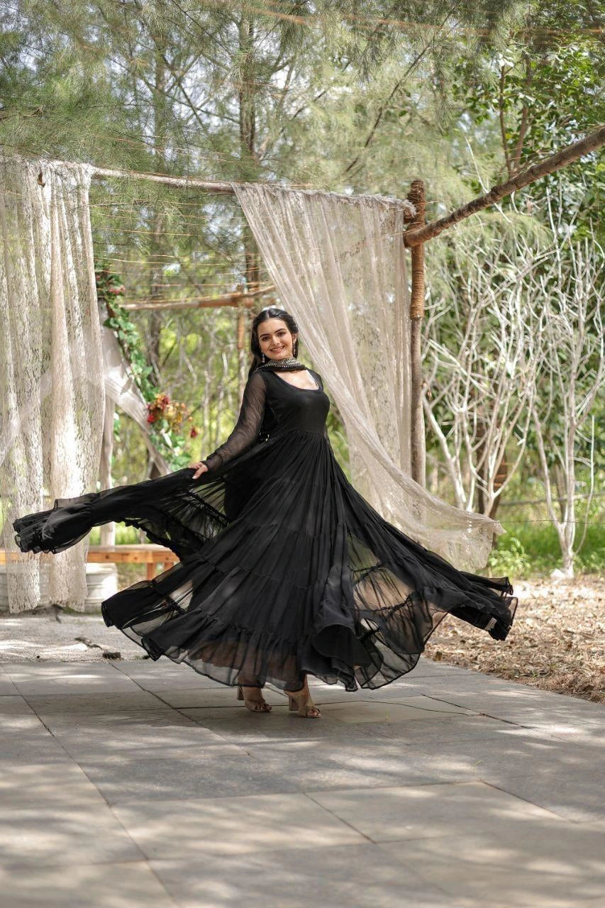 Woman in a black dress standing outdoors with curtains and trees in the background