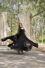 Woman in a black dress standing outdoors with curtains and trees in the background