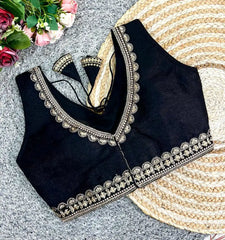 Black blouse with intricate gold embroidery on a textured surface with flowers and a fan.