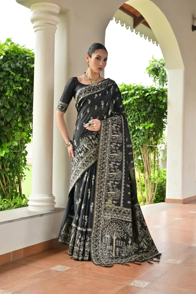 Woman wearing a black and white saree standing in an outdoor setting with greenery.