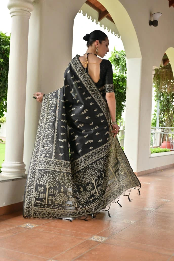 Woman holding a black and white patterned saree in an outdoor setting with columns and greenery.