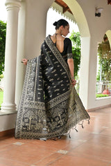 Woman holding a black and white patterned saree in an outdoor setting with columns and greenery.
