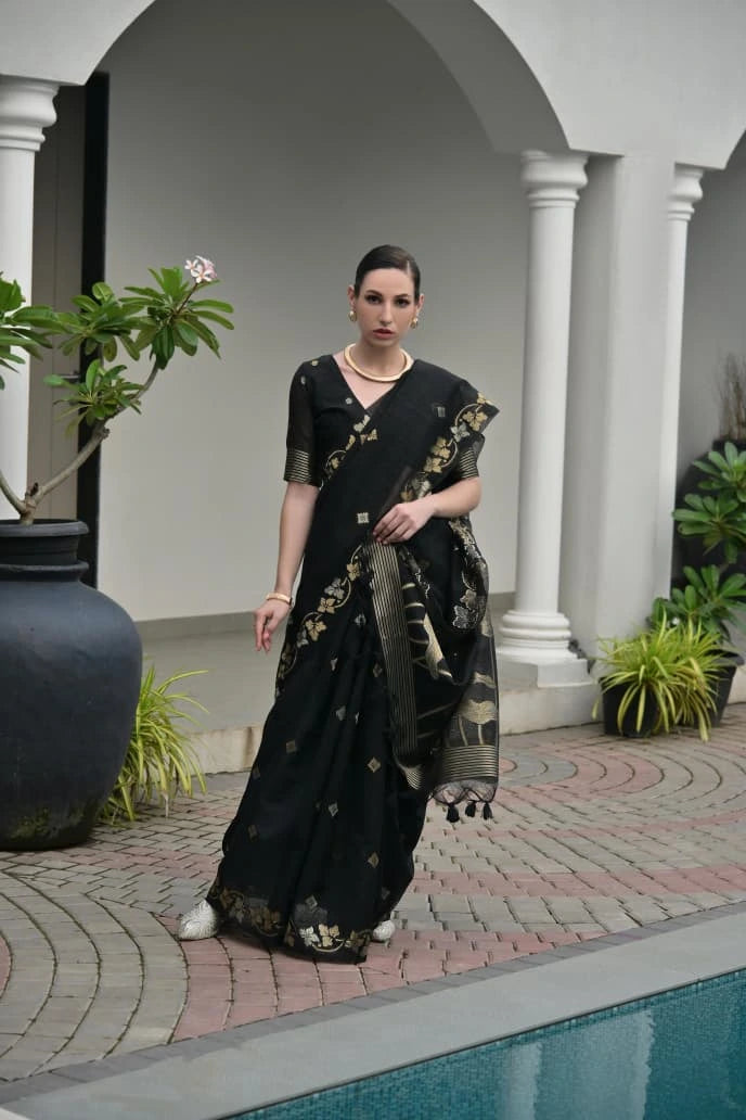 Woman in a black saree with gold patterns standing by a poolside.