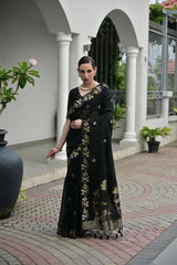 Woman in a black saree with gold patterns standing outdoors.