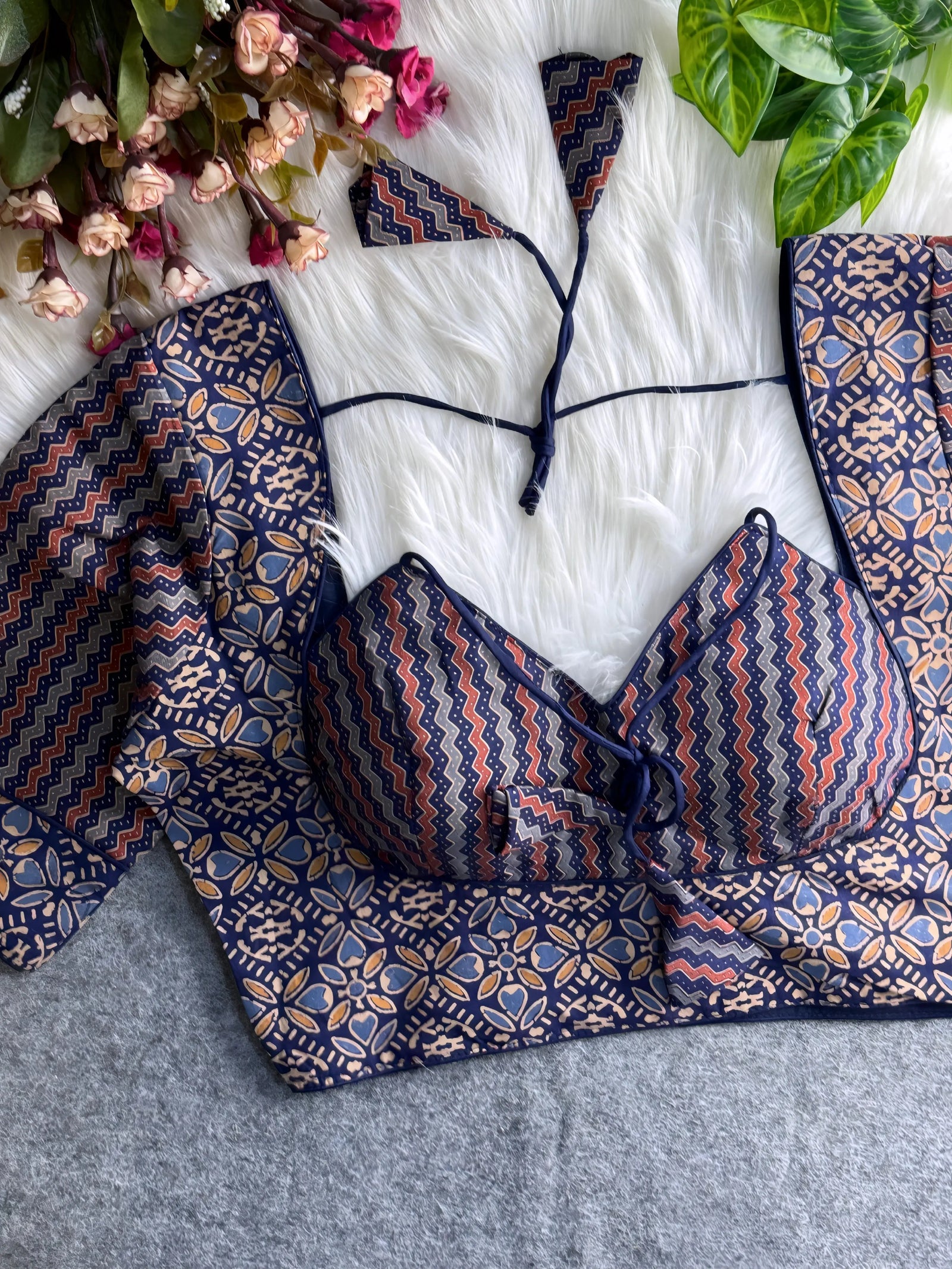 Navy and maroon printed padded blouse with geometric and floral patterns, displayed on a white fur surface with artificial flowers and green leaves in the background.