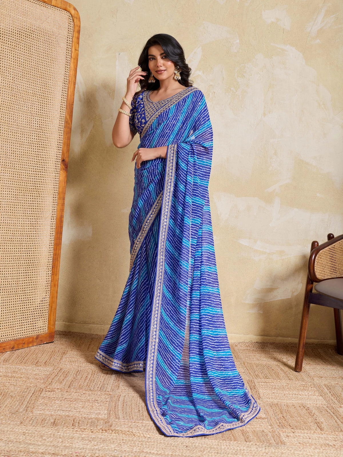 Woman wearing a blue saree with a patterned border against a beige wall.