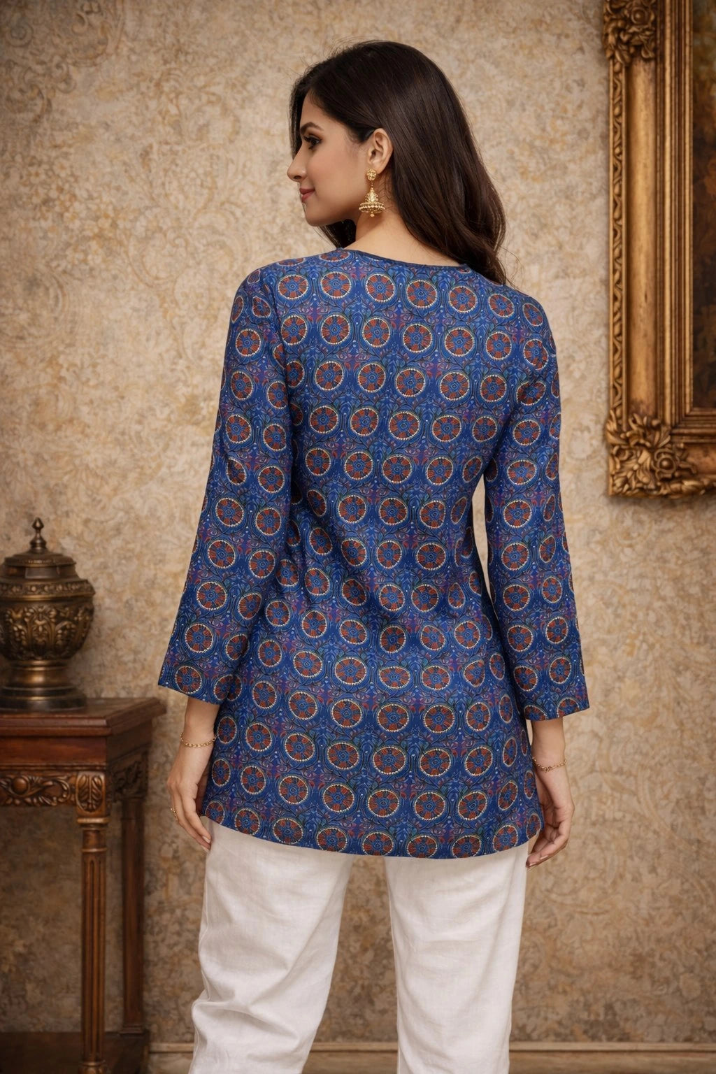 Woman wearing a blue patterned top and white pants in a room with decorative elements.