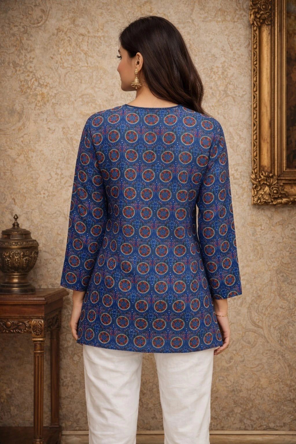 Woman wearing a blue patterned top and white pants in an elegant room.