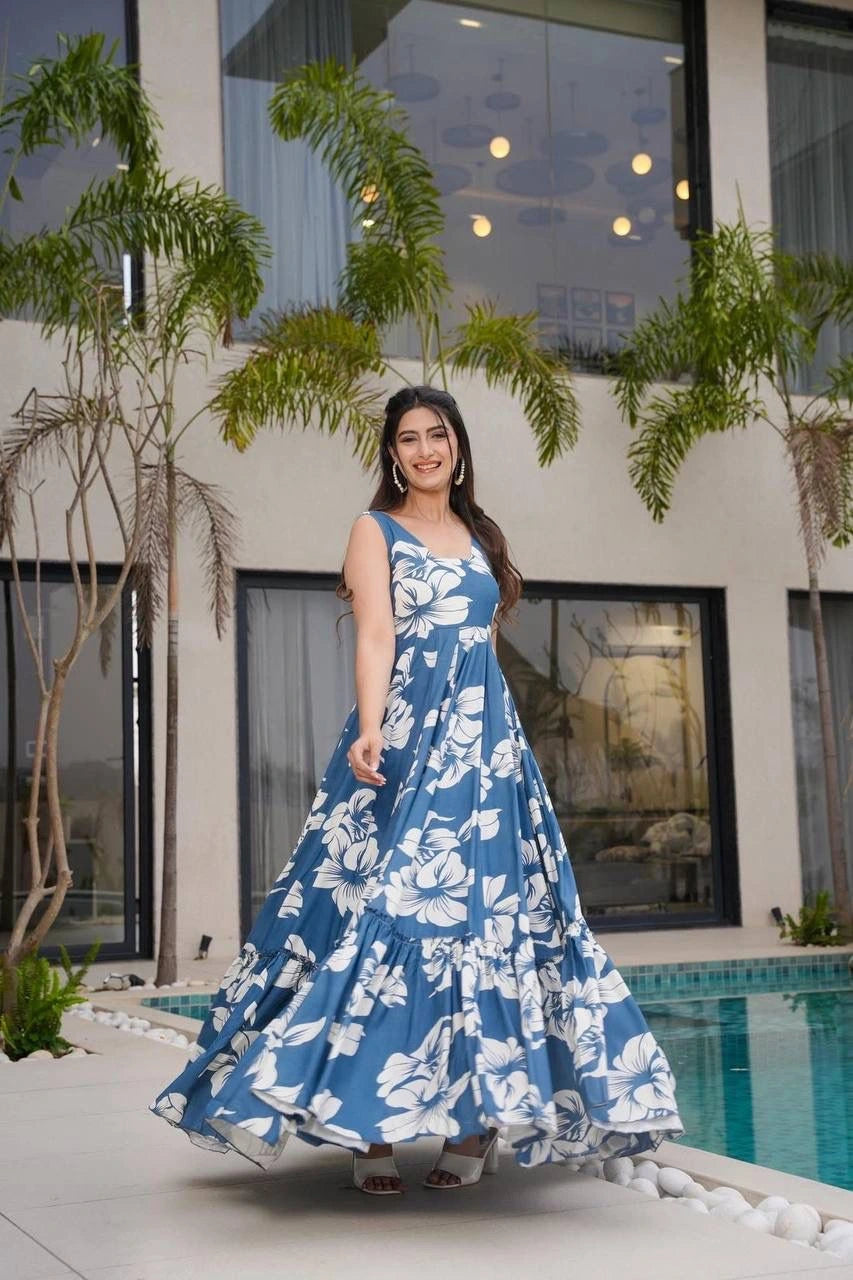 Woman in a blue floral dress standing by a pool with a building and plants in the background