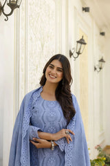 Woman in a blue outfit standing in front of a decorative wall.