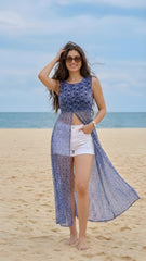 Woman in a blue floral dress and white shorts standing on a beach.
