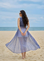 Woman in a blue dress standing on a beach with ocean in the background