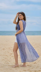 Woman in a blue patterned dress standing on a beach with ocean and sky in the background