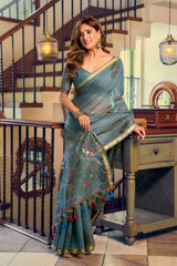 Woman in a blue saree standing in an indoor setting with decorative elements.