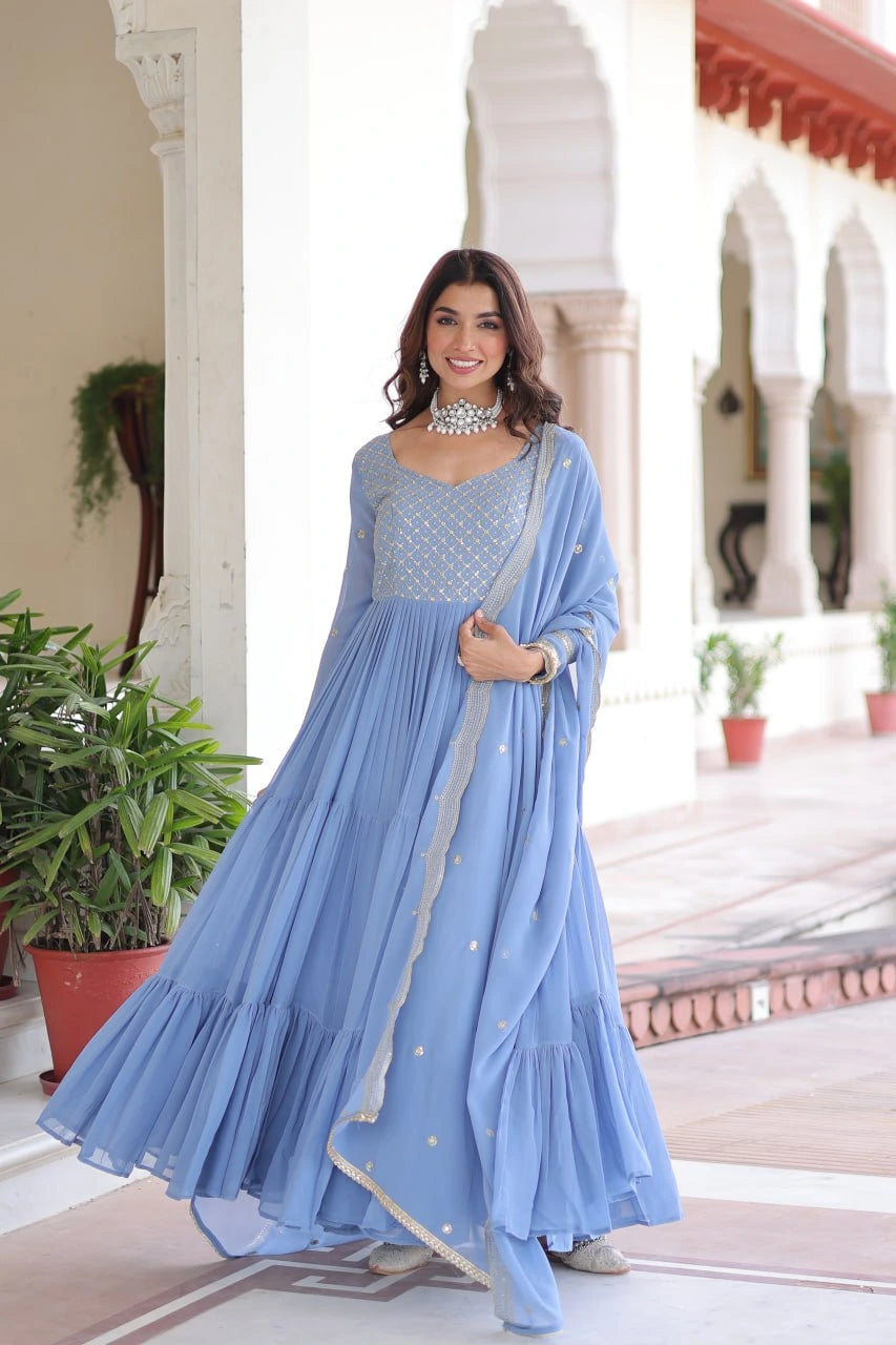 Woman in a light blue traditional outfit standing in an elegant indoor setting with plants.