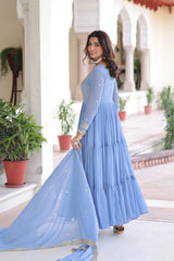 Woman in a light blue dress standing in an outdoor setting with plants and arches.