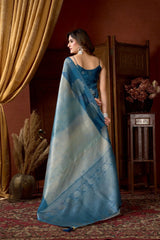 Woman in a blue saree standing in a room with decorative elements.