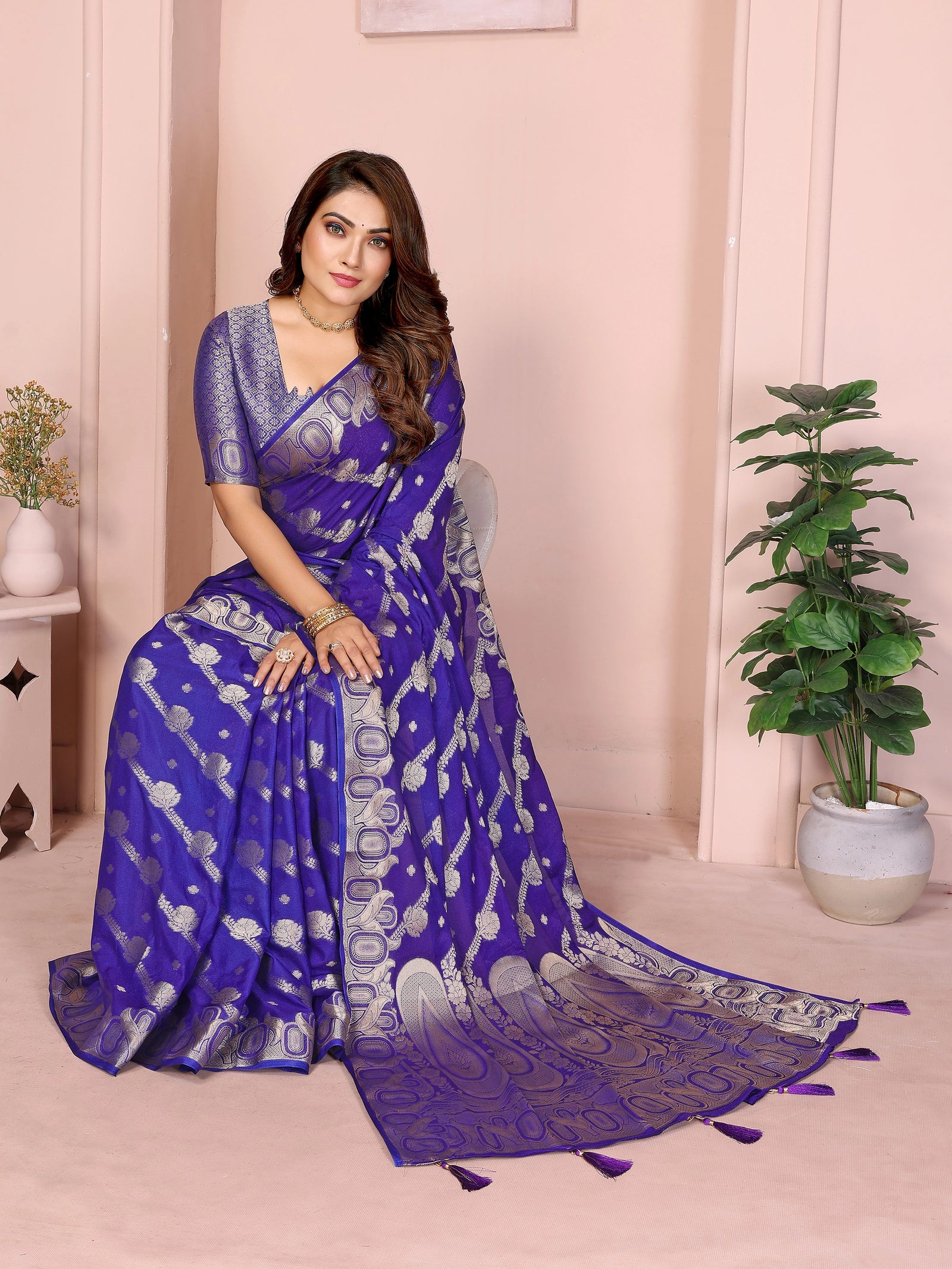 Woman wearing a blue saree with a white border in a room with plants.