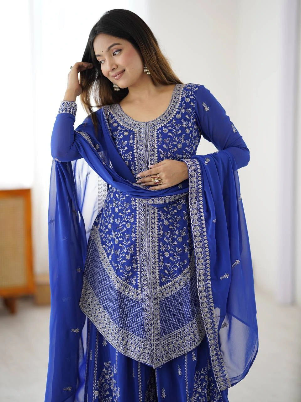 Woman wearing a blue embroidered traditional outfit with a white background
