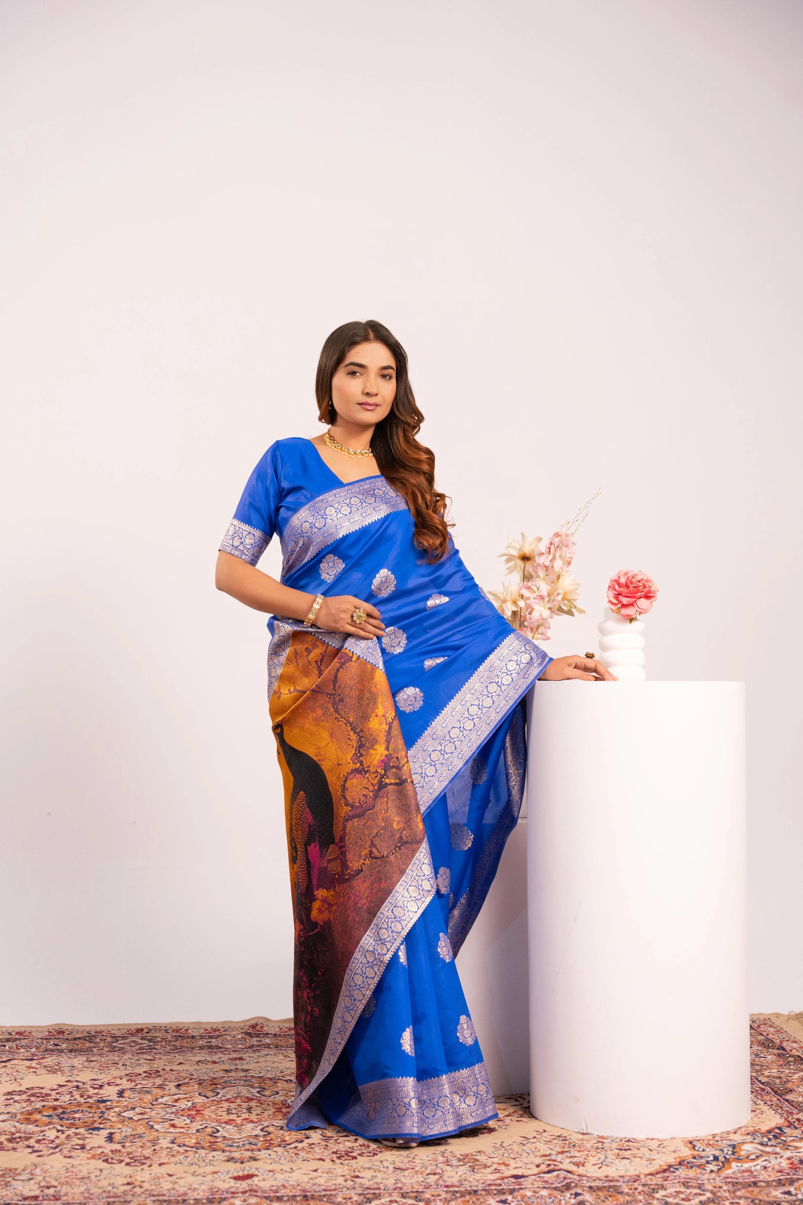 Woman wearing a blue saree with a colorful pattern, standing against a white background.