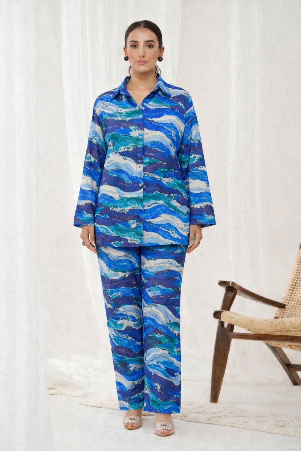 Woman wearing a blue and green patterned outfit standing in front of a white curtain.