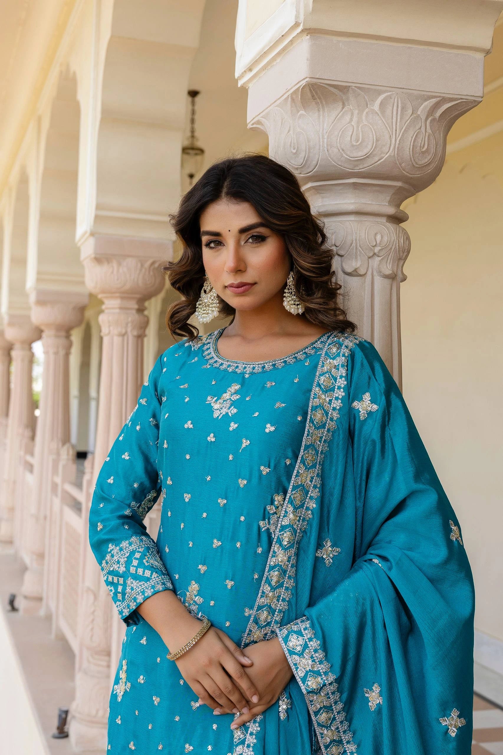 Woman in a blue traditional outfit with white patterns standing in an architectural setting.