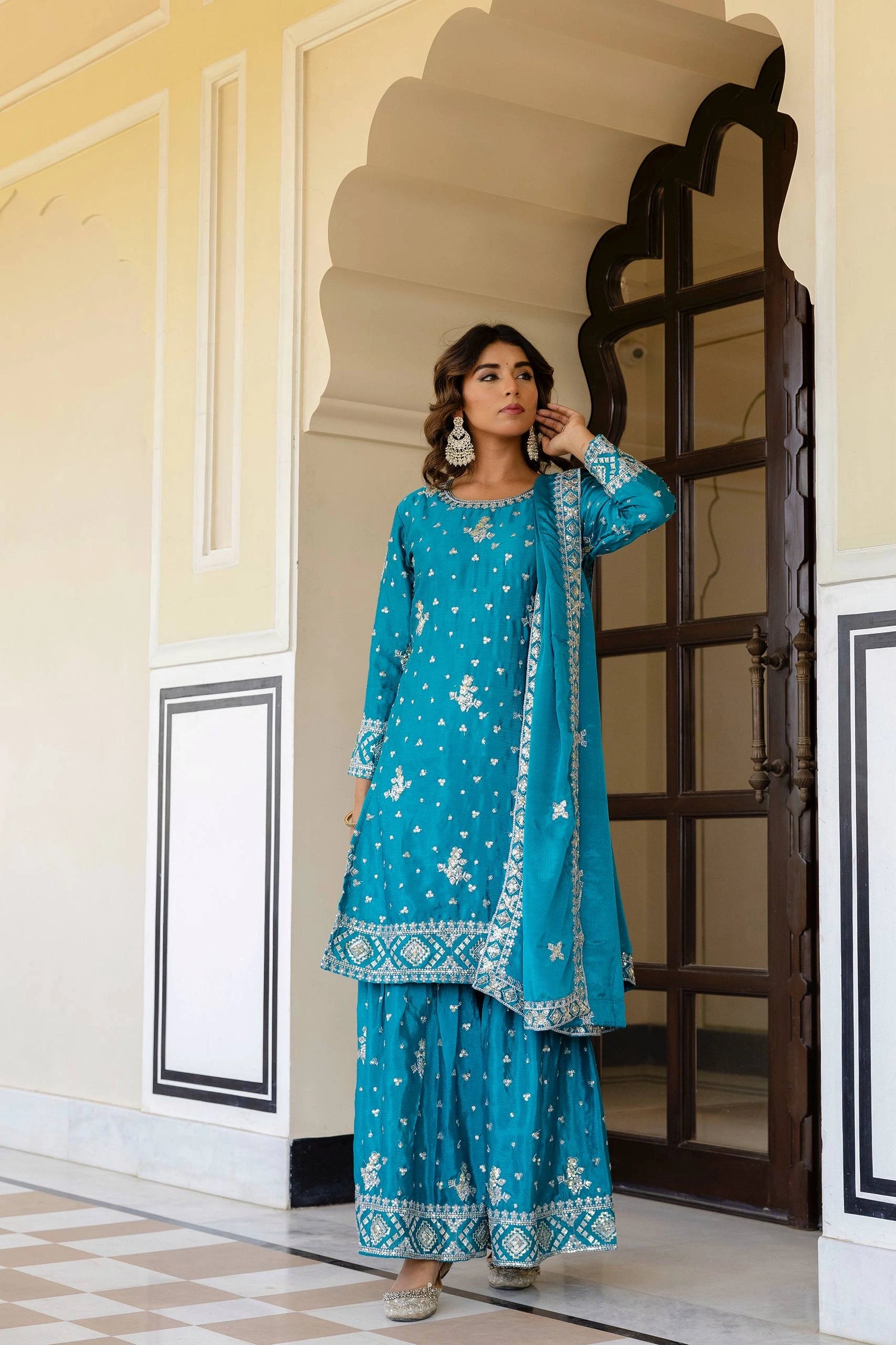Woman in a blue traditional outfit standing in an ornate doorway.