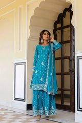 Woman in a blue traditional outfit standing in an ornate doorway.